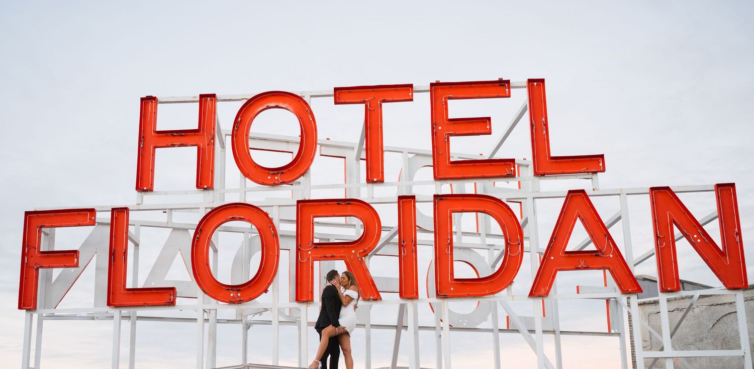 Red vintage hotel sign against bright blue sky with small figure silhouette.