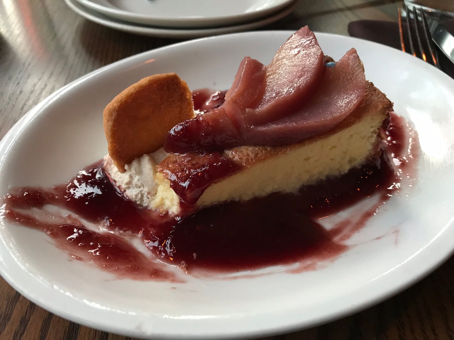 Slice of creamy cheesecake with berry sauce on white plate.