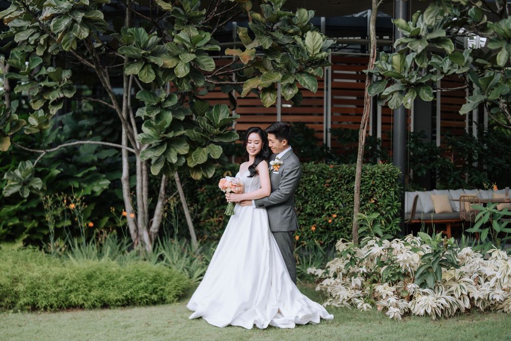 Wedding couple embraces under fig trees in an outdoor garden setting.