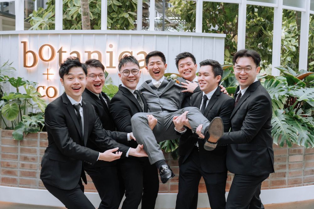 Groomsmen in dark suits playfully lift someone during wedding celebrations at Botanica.