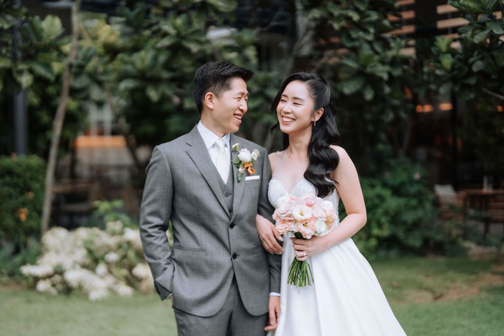 A joyful wedding couple shares a laugh together in an outdoor garden setting.