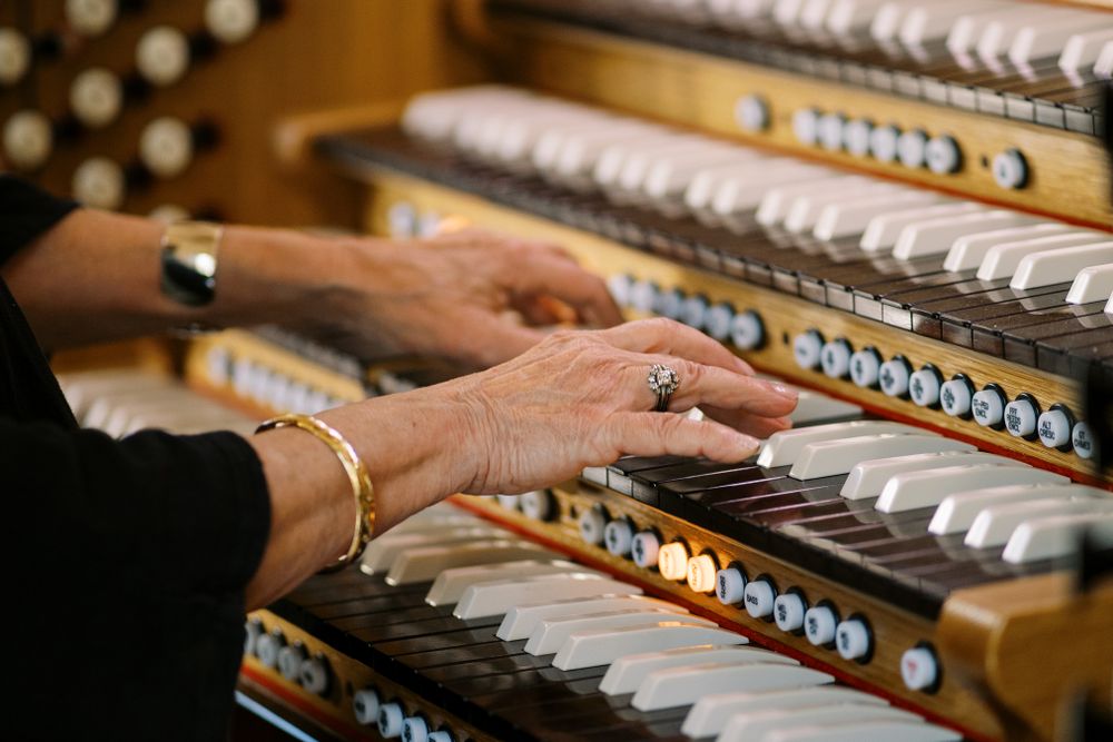 Close-up of hands playing multiple keyboards on vintage organ.
