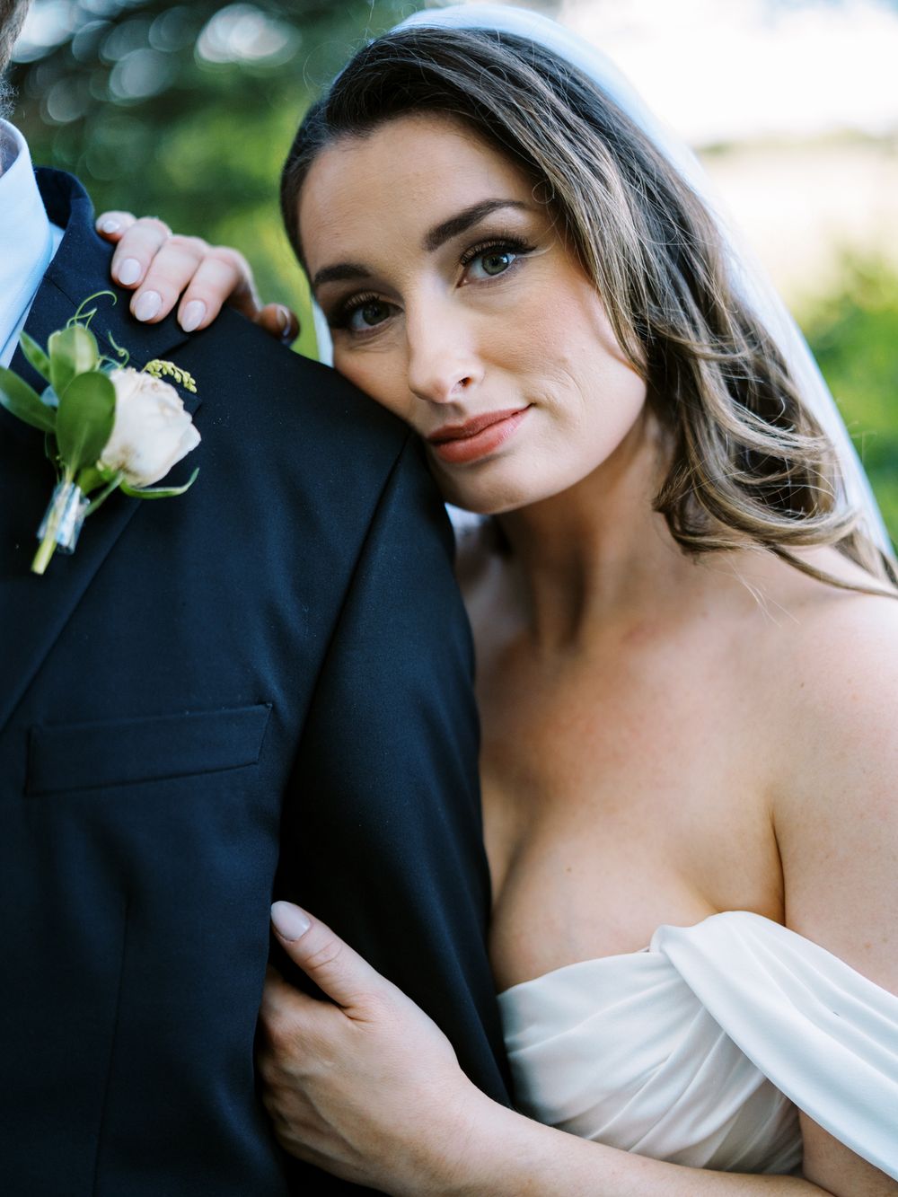 A romantic wedding portrait showing a bride in an off-shoulder gown leaning against her partner.