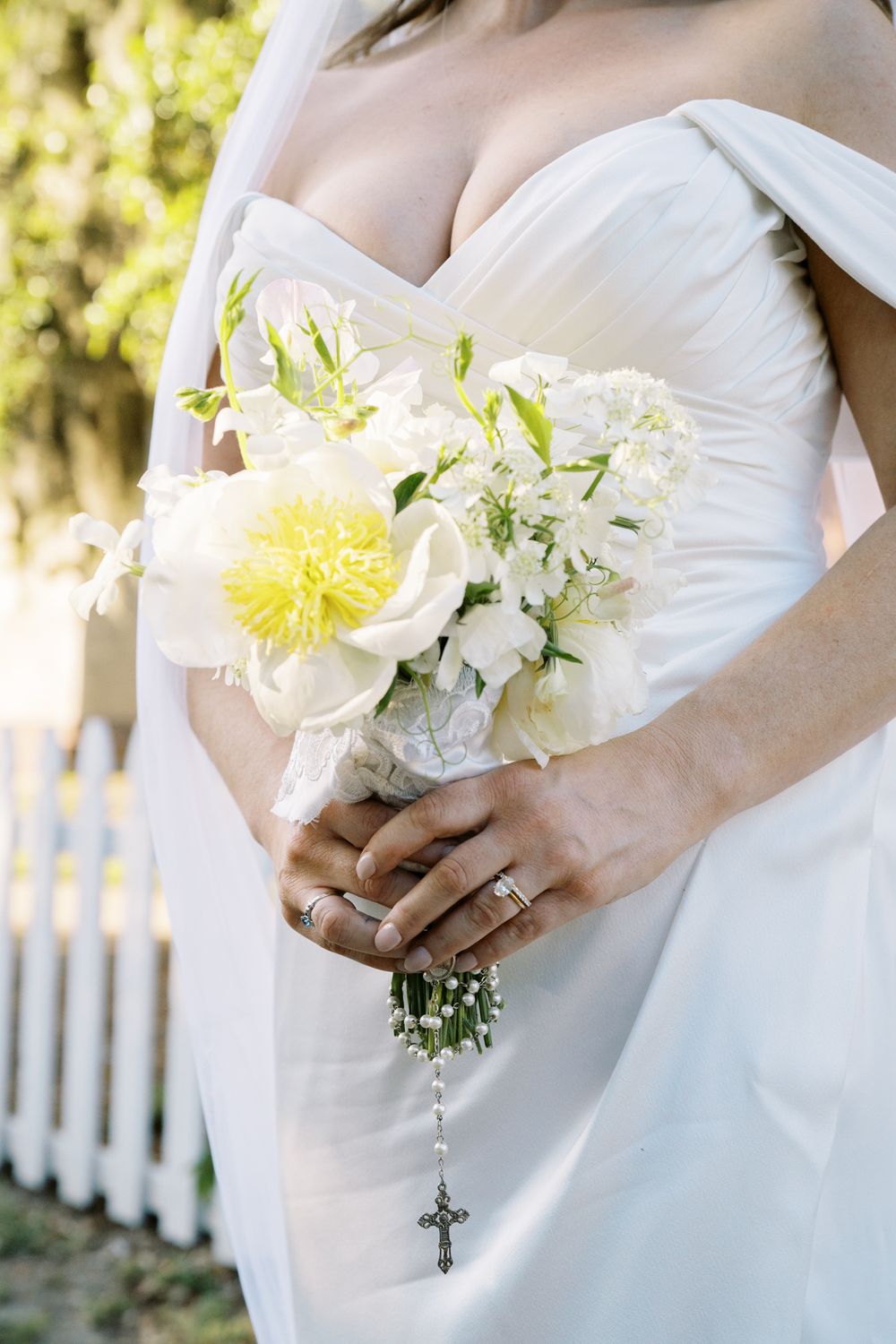 White and yellow bridal bouquet with cross charm against wedding dress.