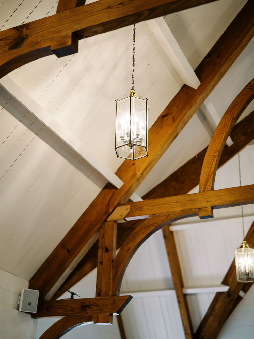 Rustic wooden ceiling beams and elegant glass pendant lighting in a white vaulted chapel ceiling.