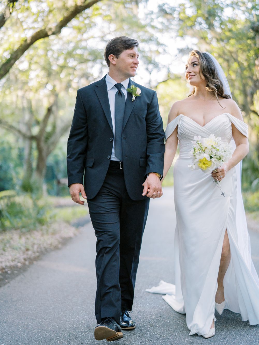 A couple walking together on a garden path, with the bride carrying a white bouquet.