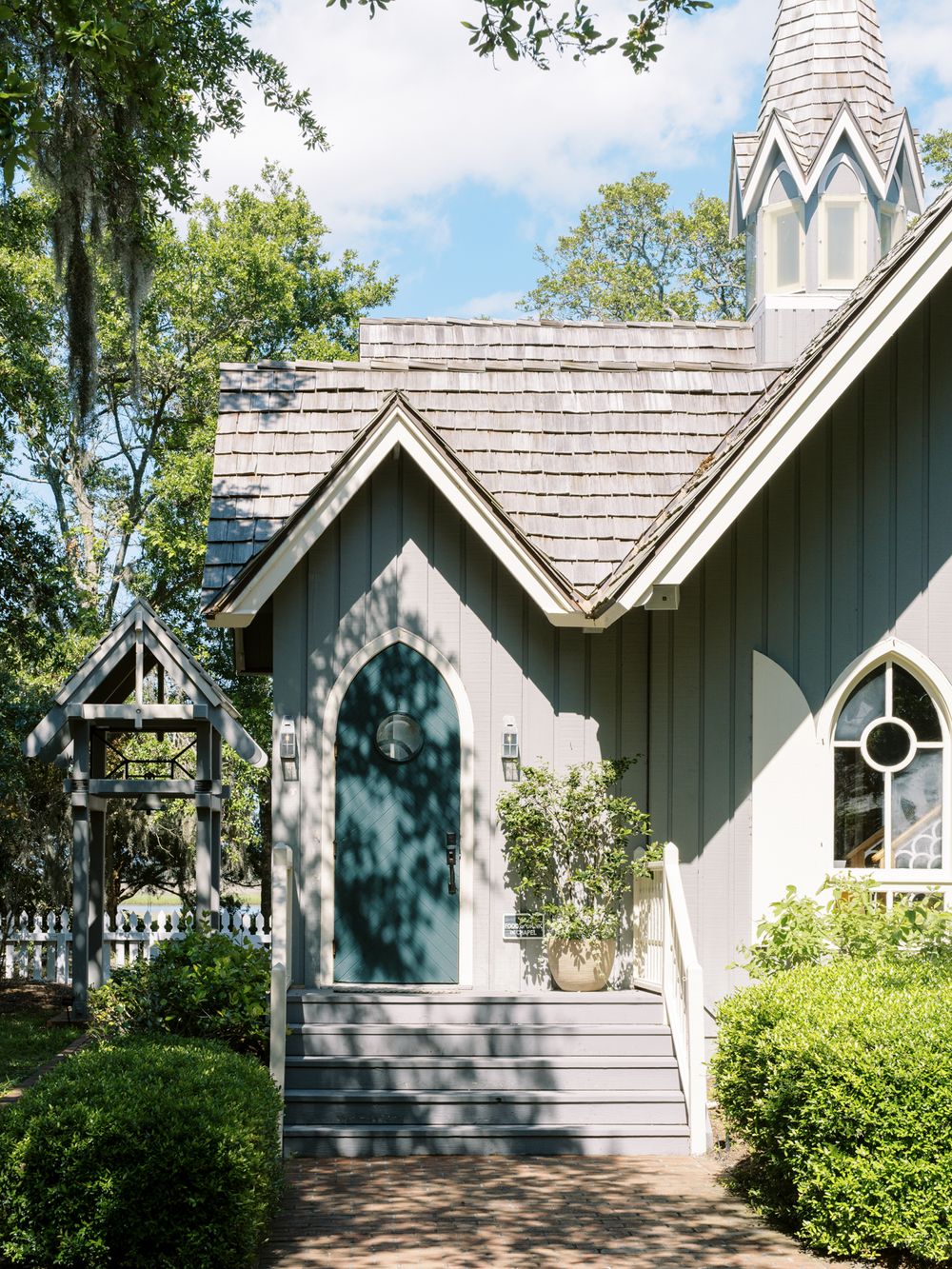 Small white chapel with Gothic architecture features and a pointed spire set among trees and landscaping.