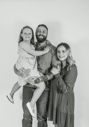 Black and white studio portrait of a family of three posing together against a light background.