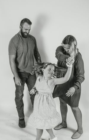 Black and white studio portrait of a family dancing and laughing together against a light background.