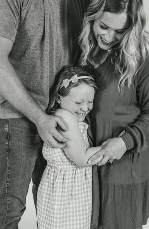 Black and white candid family moment showing a young child in a checkered dress laughing while being embraced.