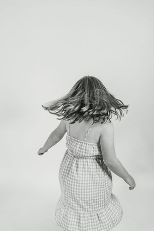 A person in a checkered dress twirls and spins with their hair flowing in a sequence of black and white photos.