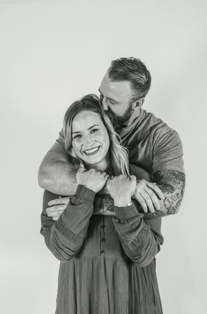 Black and white portrait of a couple embracing and laughing together against a light background.