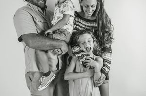 Black and white photo collage showing candid family moments with parents and young children embracing and playing together.