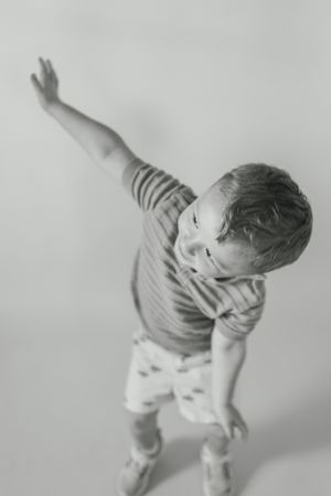 Black and white photo of a young child in a striped shirt dancing and reaching upward with one arm.