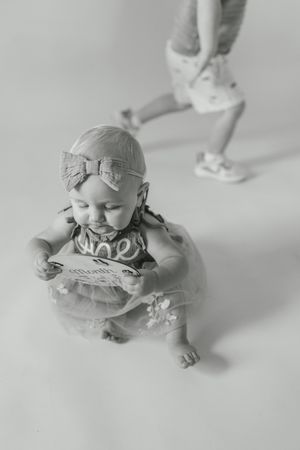 Black and white series of a baby in a dress sitting and playing on a light background.