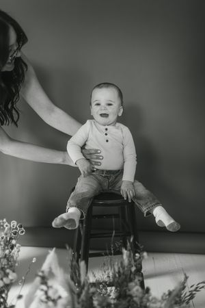 A series of black and white photos showing a baby sitting on a wooden chair with floral decorations below.
