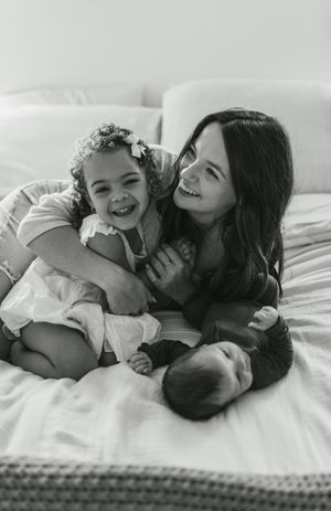 Black and white photo series of mother and child sharing joyful moments while cuddling together on white bedding.