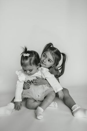 Black and white photo series showing two children lying down and interacting playfully together on a white surface.