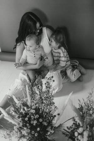 A black and white intimate family moment with small children sitting together on the floor with flowers in the foreground.