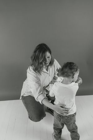 A parent and child share a playful moment in a minimalist white room, creating a tender black and white scene.