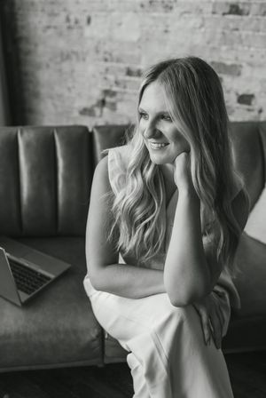 A black and white photo series shows a person with wavy hair laughing while seated on a couch against a brick wall.
