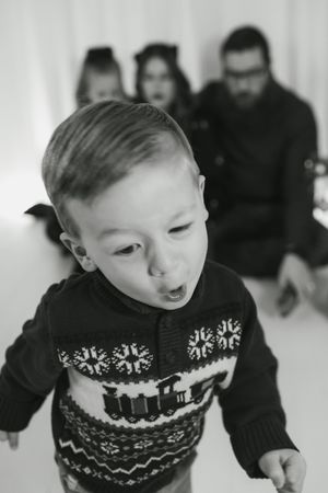 A sequence of black and white photos showing a child in a patterned winter sweater making playful expressions.