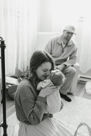 Intimate family moment captured in monochrome showing gentle interaction on floor near window.
