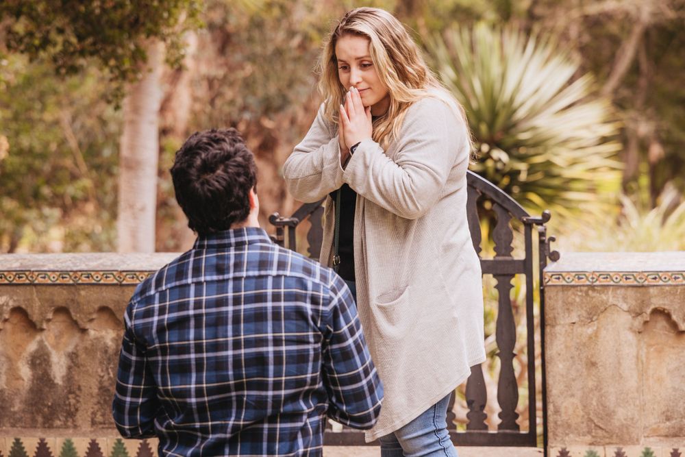 Romantic proposal moment captured in front of ornate stone architecture.