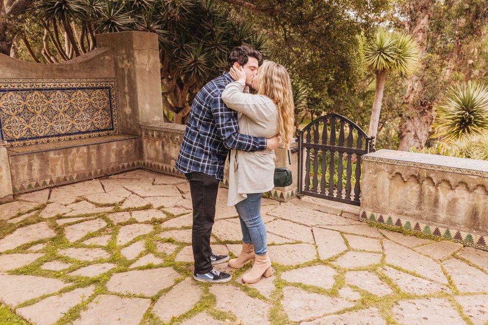 Couple sharing a tender moment on decorative stone pathway surrounded by foliage.