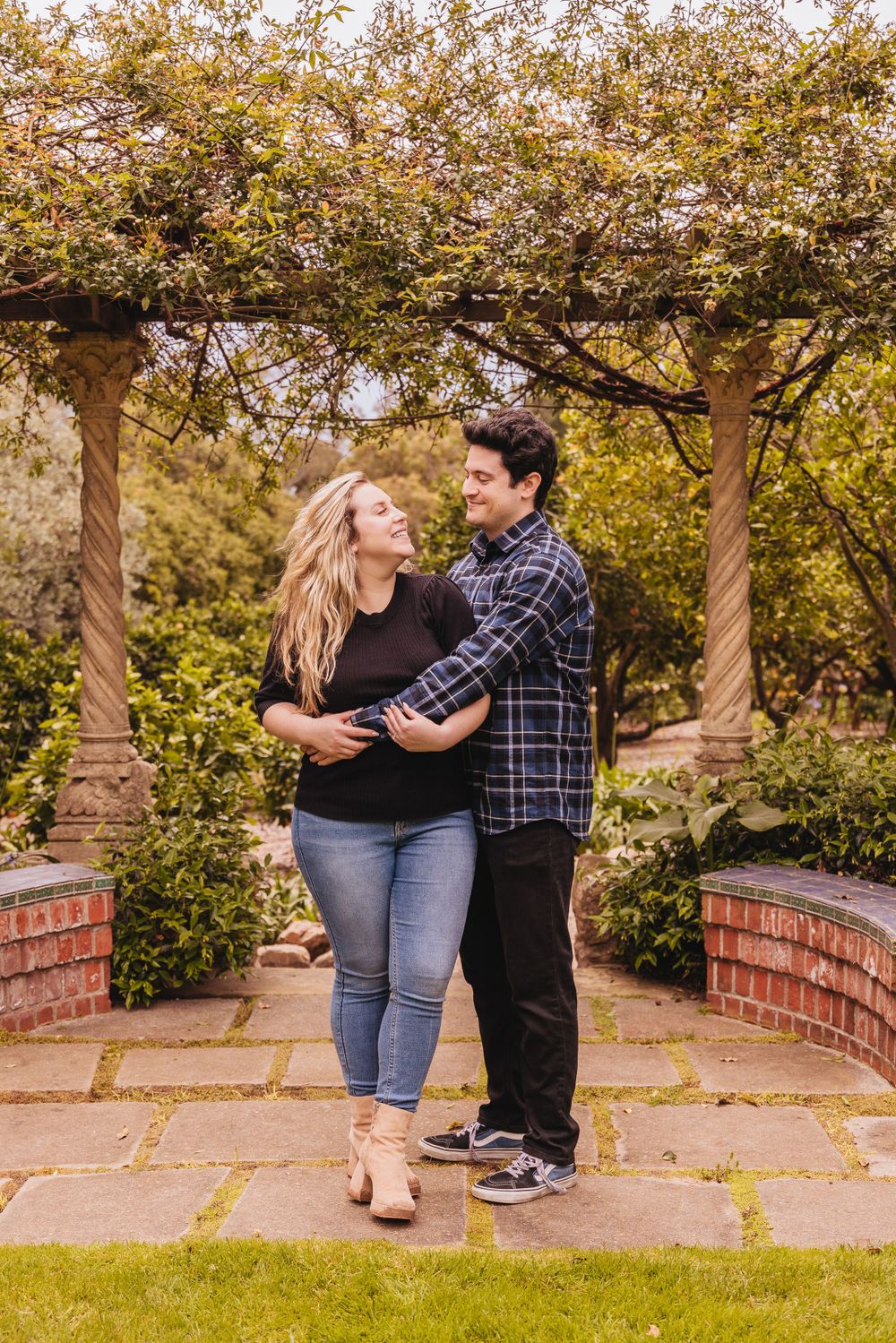 Couple sits together on brick wall in garden setting during autumn.