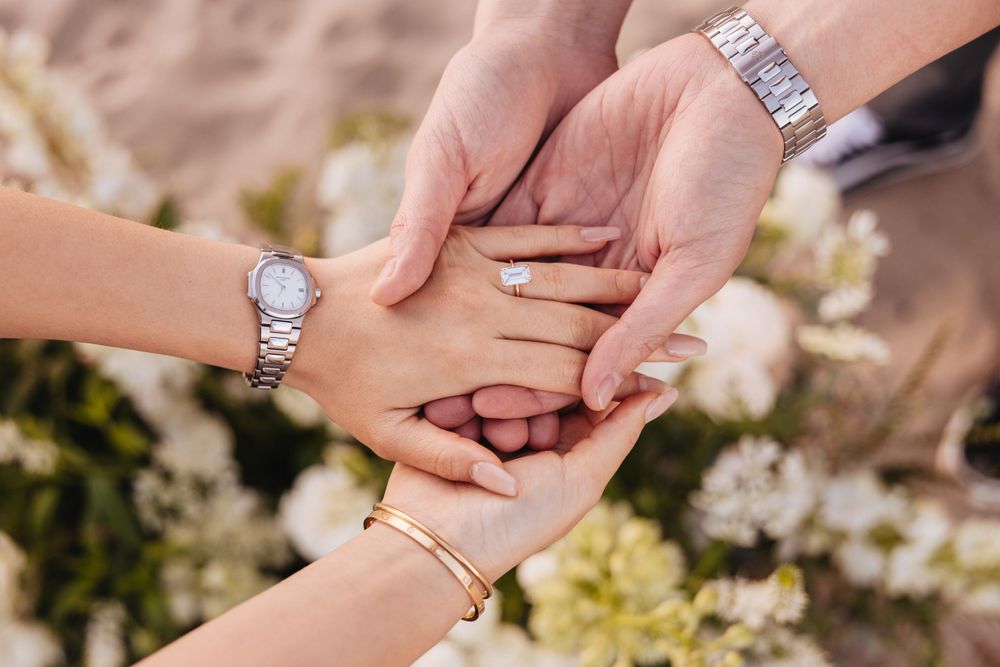 Close-up of hands showing engagement rings against white spring blossoms.