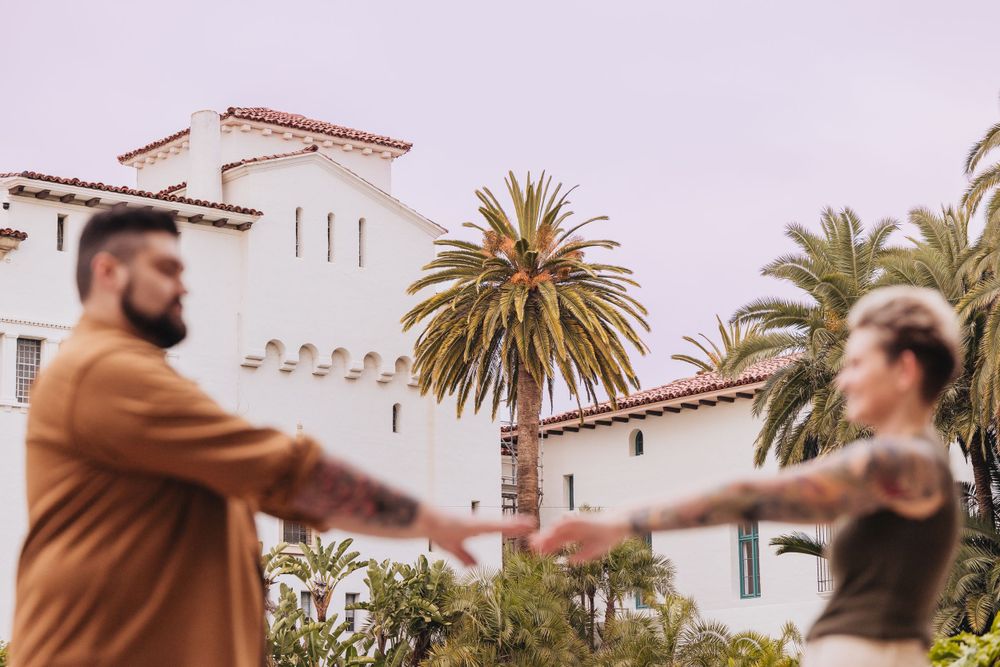 Couple dancing in front of a Spanish-style building with palm trees.