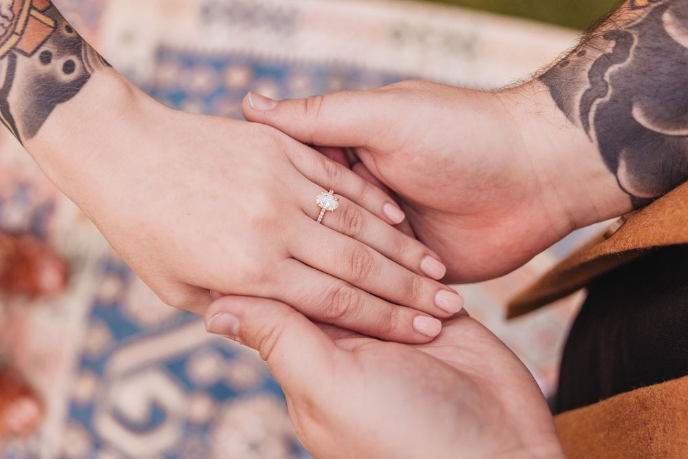 Close-up of tattooed hands with engagement ring showing tender moment.