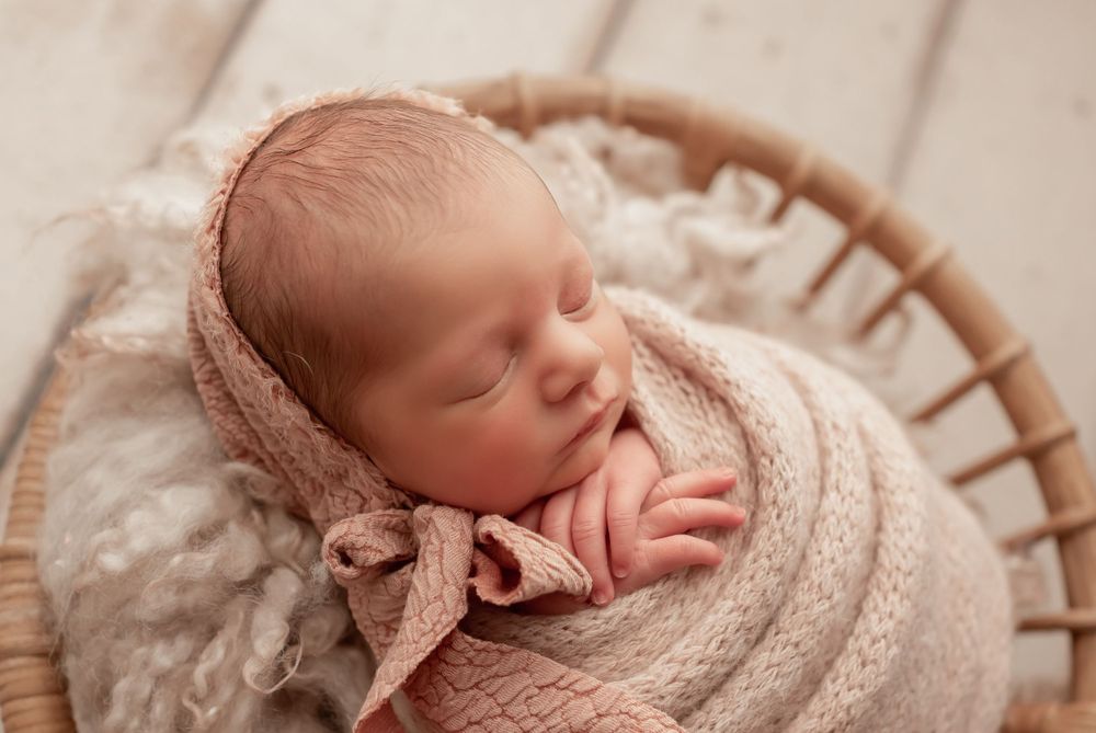 Newborn baby wrapped in beige knit wrap with bow detail sleeping peacefully.