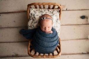 Sleeping baby wrapped in navy swaddle on floral cushion in wooden chair.