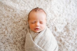 Swaddled newborn baby sleeping peacefully on white textured background.