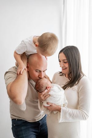 Family playing and showing affection with their young child against white backdrop.