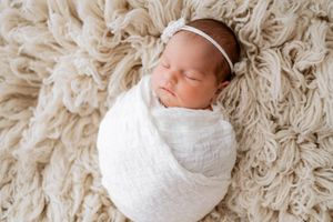 Sleeping newborn baby peacefully wrapped in white blanket on textured beige shag rug.