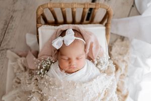 Newborn photography session with delicate white wraps and floral headpieces on pink backdrop.