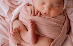 A newborn baby wearing pink swaddle wrap lying on soft fabric background during professional photoshoot.