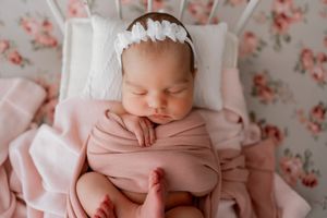 Newborn baby wrapped in pink swaddle blanket sleeping peacefully against floral backdrop.