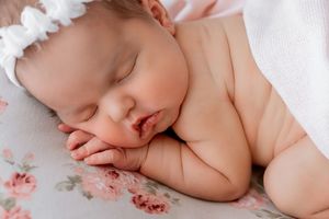 Sleeping newborn rests peacefully on floral patterned blanket in soft lighting.