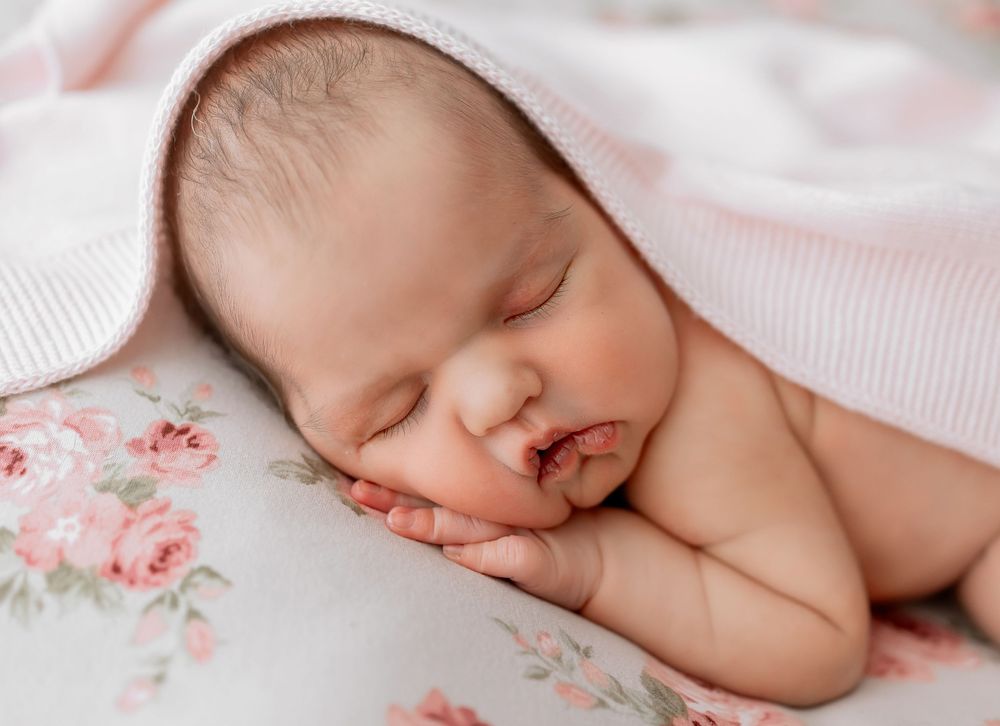 Peaceful sleeping newborn rests on floral cotton bedding with white blanket detail.