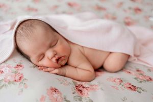 Newborn photography series showing baby sleeping peacefully on pink floral backdrop.