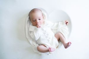 Newborn baby swaddled in soft white fabric against white background during professional photoshoot.