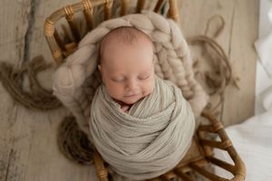 Newborn baby peacefully sleeping while wrapped in soft beige swaddling blanket during professional photo session.