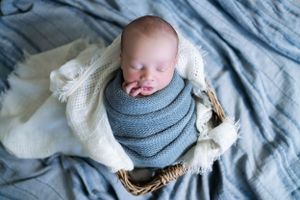 Infant resting on blue textured blanket with gray wrap during artistic newborn portrait session.