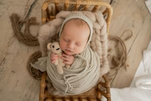 Overhead view of sleeping newborn wrapped in neutral knit fabric on rattan chair.