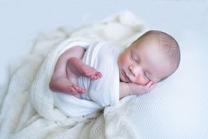 Peaceful sleeping newborn posed on white textured backdrop during professional photo session.