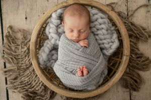 A collection of newborn photography images showing a sleeping baby wrapped in gray fabric in round wooden baskets.
